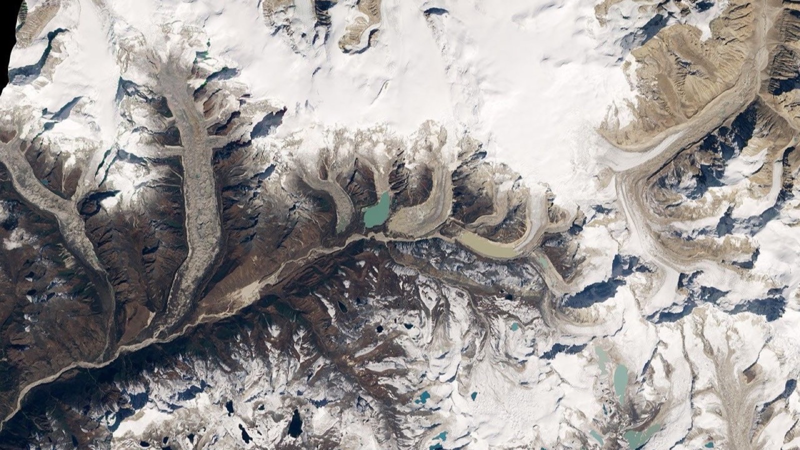 Natural-color satellite photograph of the Bhutan Himalaya: debris-covered glaciers threading down valleys between snow-covered peaks, with small turquoise meltwater lakes pooling at their lower ends